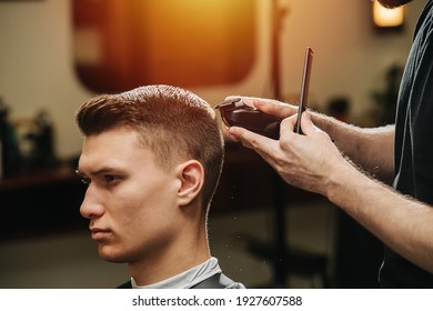 Male hairdresser making a haircut for a young man in a barber shop. He's standing behind client, finishing work with hair clipper. Close up, cropped. - Powered by Shutterstock