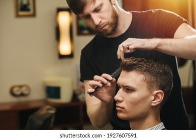 Male hairdresser making a haircut for a young man in a barber shop. He's standing behind client sitting in a chair, combing hair. - Powered by Shutterstock