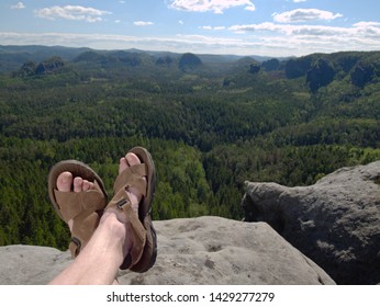 Male Hairy Legs With Sandals Rest On Rocky Summit Above Valley Of Natural Park. Lazy Sunny Summer Day.