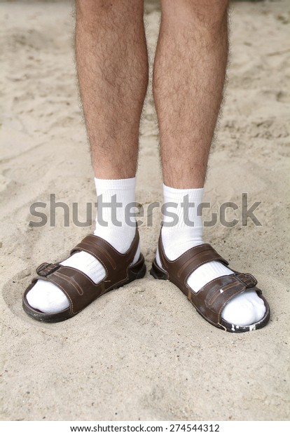 Male hairy legs in white socks in sandals in sand\
on beach\
