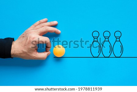 Male hand is about to flick the ball and knock or strike the bowling pins in a row.

