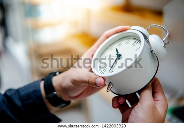 Male hand adjusting or changing the time on\
white clock. Time management\
concept.
