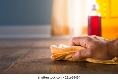 Male hand applying wood care products and cleaners on hardwood floor surface.