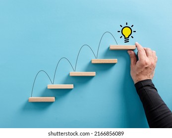 Male hand arranges a wooden block ladder with idea light bulb symbol. Ladder of success, brainstorming, reaching to an idea or idea generation concept. - Shutterstock ID 2166856089