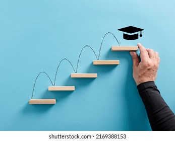 Male hand arranges a wooden block ladder with academic cap symbol. Graduation achievement and education goals. - Shutterstock ID 2169388153