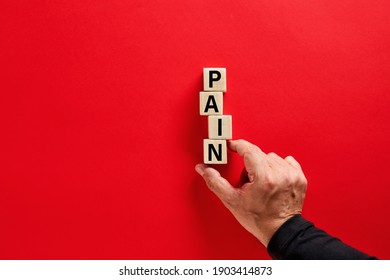 Male hand arranging the wooden blocks with the word pain on red background with copy space. Emotional, psychological or physical pain concept.