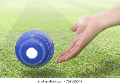 A male hand bowling and releasing a blue wooden lawn bowling ball on a green lawn grass surface -3D render