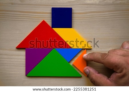 male hand build model of House Made Of Wooden colorful Tangram Puzzle. isolated on wooden board background.