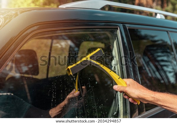 Male hand with car rubber cleaner cleaning and\
washing automobile side\
window.