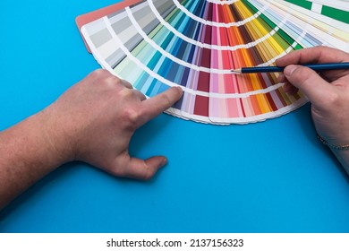 Male Hand Choosing Paint Tone At Color Sampler Isolated On Blue Background.  Different Colors 