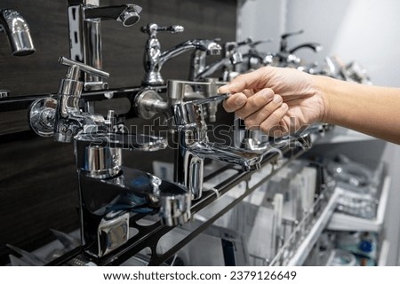 Male hand choosing stainless steel chrome water tap in home design store. Plumbing fixture selection for bathroom. Home improvement concept