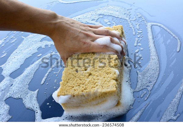 male hand is cleaning  car bonnet with yellow\
sponge; selective focus at\
hand