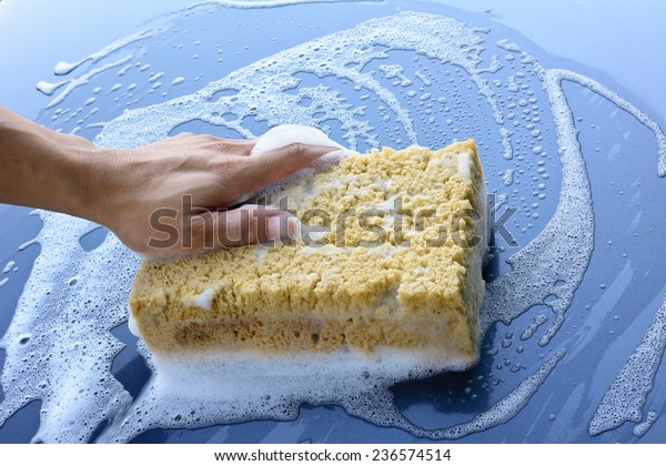 male hand is cleaning  car bonnet with yellow\
sponge ; selective focus at\
hand