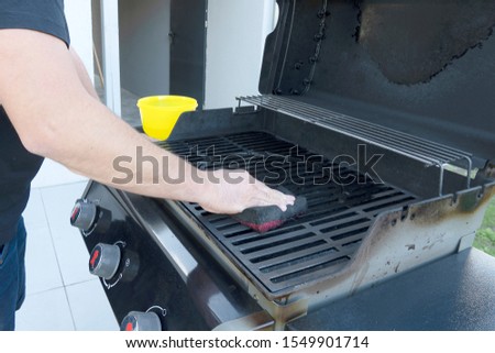 The male hand cleans the black grill with a soft brush. Grill for frying meat. Cleaning the outdoor gas grill in the backyard.