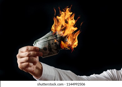 Male hand close-up, holds burning money in hands, burning US dollars. Black background, isolate. The concept of inflation, a decrease in the purchase of foreign currency, and devolution.