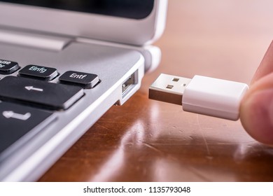 Male Hand Connecting A White USB Cable To The USB Port Of A Small Notebook