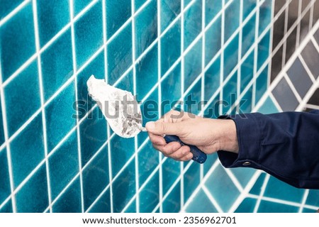 Male hand construction worker using trowel or building spatula spreading cement grout on blue ceramic tiles in the swimming pool