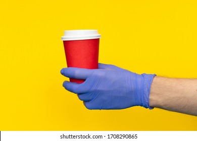 Male Hand Courier Wearing Medical Gloves Holding Paper Cup Coffee For Take Away Isolated On Yellow Background. Contactless Delivery Service In Quarantine Coronavirus Pandemic. Volunteer Make Donation