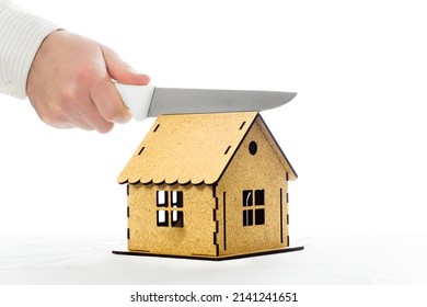 Male hand cutting a miniature house model with a kitchen knife in half. Home division in a divorce. - Shutterstock ID 2141241651