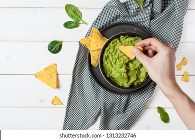 Male hand dipping nachos in guacamole sauce - Shutterstock ID 1313232746