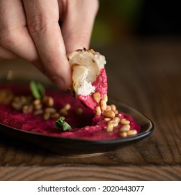 Male Hand Dipping Piece Of Pita Bread Into Bowl With Red Hummus Or Dipping Sauce. Beetroot Puree With Peanuts, Close-up Shot. Soft Focus. Copy Space.