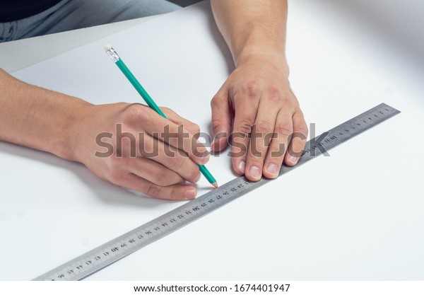 Male hand draws pencil under a ruler on a white\
sheet of paper