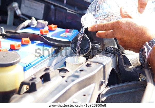 male hand filling washer fluid reservoir cap in\
engine room with bottled\
water