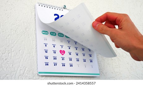 A male hand flipping a January page of the wall calendar 2024 showing the upcoming St Valentine's Day date on the next one - Powered by Shutterstock