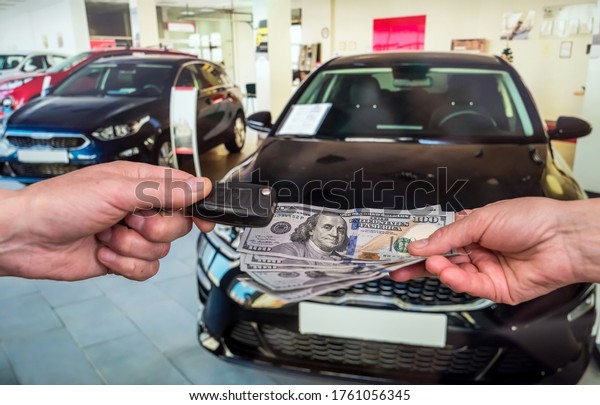 Male hand gives money and take car keys, new car\
as background. finance