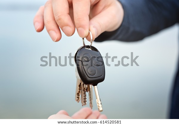 Male hand giving car and house keys to female,\
close-up photo, outdoor,\
daytime