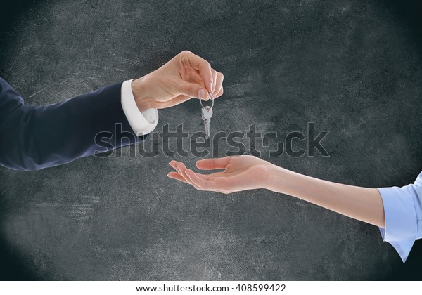 Male hand giving a car key to woman\'s hand on\
grey background