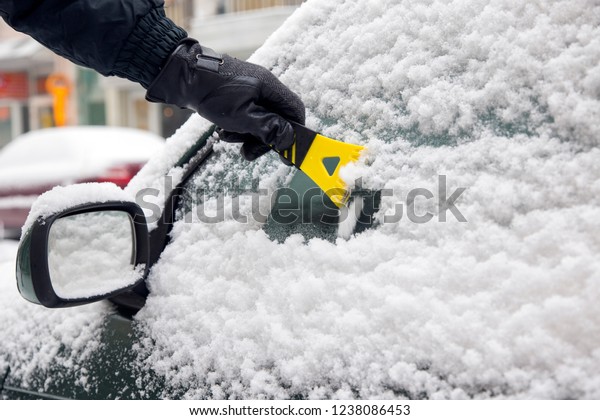 Male hand with\
glove cleaning snowy car\
window
