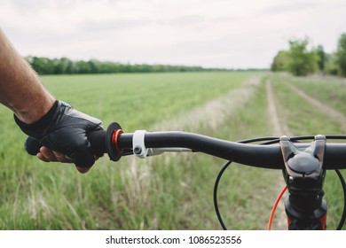 Male Hand In Glove Holding Bicycle Handlebar. Riding A Bike First Person Perspective. Sports, Tourism And Activity Concept