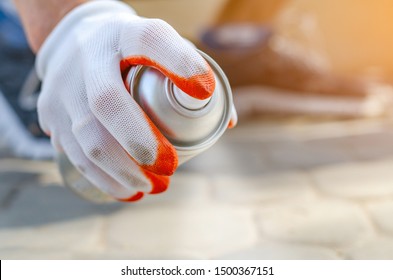 Male hand in a glove holds an aerosol spray can with white paint, colors. Surface painting, graffiti on the street. - Powered by Shutterstock