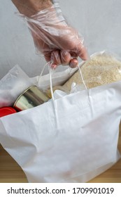 A male hand in a glove holds a white bag with a food set. Dry rations. Rice, milk, canned food, jam. Quarantine food delivery - Shutterstock ID 1709901019