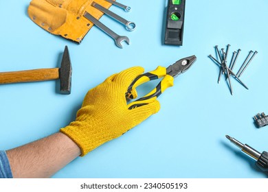 Male hand in gloves holding pliers near different instruments on blue background