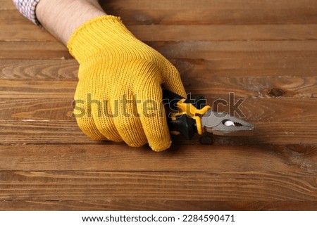 Male hand in gloves holding pliers on wooden background