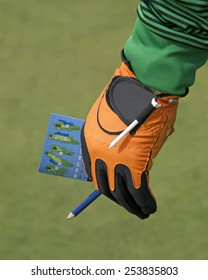 Male Hand With Golf Score Card Keeping Score. Holding The Score Card Off To The Side While His Buddies Golf, Ready To Keep Track