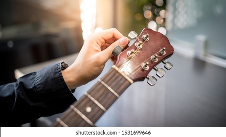 Male hand guitarist adjusting pegs on acoustic guitar during music lesson at home. String musical instrument concept - Shutterstock ID 1531699646