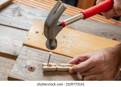 Male Hand Hold Hammer And Nail A Clothespin, Wooden Work Bench Table Background. DIY, Home Repair And Fix.