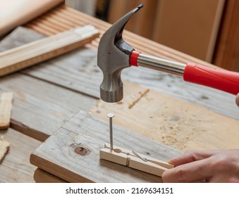 Male Hand Hold Hammer And Nail A Clothespin, Wooden Work Bench Table Background. DIY, Home Repair And Fix.