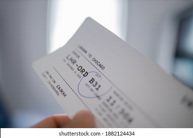 Male Hand Holding Airline Ticket With Airplane Window As Background. Close-up Of Hand Holding Plane Ticket To Chicago With Blurry Background. Travel And Transportation