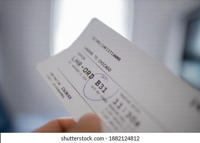 Male Hand Holding Airline Ticket With Airplane Window As Background. Close-up Of Hand Holding Plane Ticket To Chicago With Blurry Background. Travel And Transportation