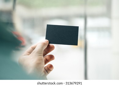 Male Hand Holding Black Business Card On The Window Background