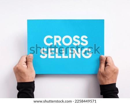 Male hand holding a blue paper with the word cross selling. Selling different products or services to an existing customer.