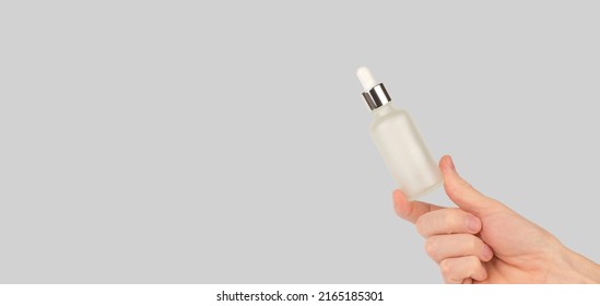 Male Hand Holding A Bottle Of Hair Serum. White Cosmetic Bottle With A Pipette In A Man's Hand.