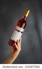 Male hand holding bottle of pink red wine, natural fruit alcohol liquor with empty label on grey background. Mock up, template for brand, vertical shot