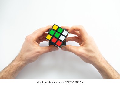 Male Hand Holding Colorful Rubik's Cubes On White Background. Rubik's Cube Was Invented In 1974 By Hungarian Sculptor And Professor Erno Rubik. Concept Of Idea And Puzzle Construction.