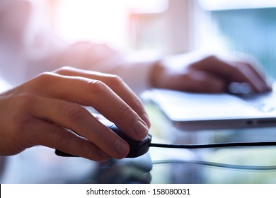 Male hand holding computer mouse with laptop keyboard in the background - Shutterstock ID 158080031