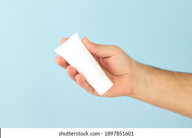 Male hand holding cosmetic skin care cream tube on light blue background close-up, mock-up for your design